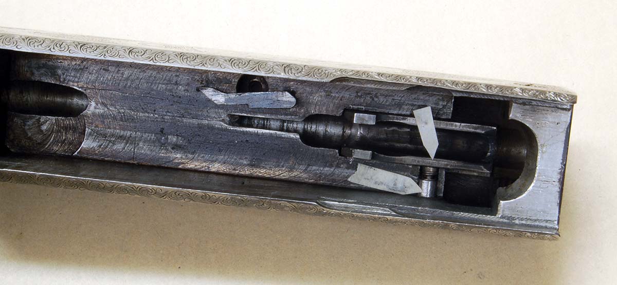 The last cartridge stop uses a spring and a plunger (long arrow). Its tip protrudes through the cartridge guide (short arrow).